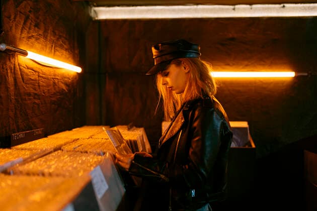 IMAGO Creative: Retro-Revival Side view of young female in black cap choosing vinyl record while standing near counter with collection of musical albums in store with glowing lamps PabloGallardo_VinylStore_14.jpg Copyright: xPabloxGallardox Model Released