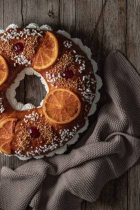 Overhead of king s cake with cream and sprinkles decorated with orange slices and cherries and placed on wooden surface near towel PimientaDulce_RosconOfKings_2.jpg Copyright: xPimientaxDulcex Model Released