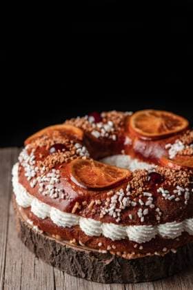 King s cake with cream and sprinkles decorated with orange slices and cherries and placed on wooden table PimientaDulce_RosconOfKings_4.jpg Copyright: xPimientaxDulcex Model Released