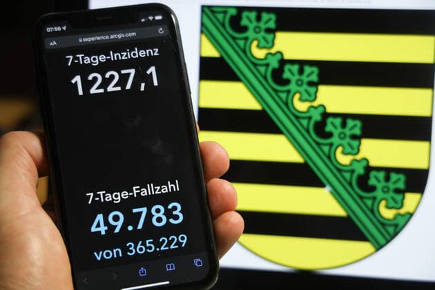 Coronavirus in Deutschland - Covid-19-Dashboard des Robert Koch-Institut DEU, Deutschland, Sachsen 05.12.2021: Die 7-Tage-Inzidenz für das Bundesland (Fälle letzte 7 Tage 100.000 EW) wird auf einem iPhone angezeigt, im Hintergrund das Landeswappen