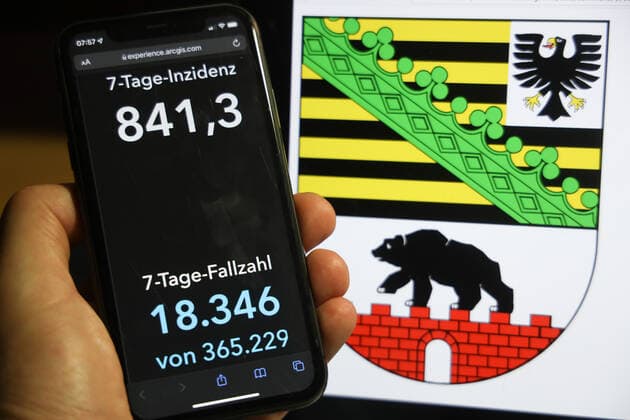 Coronavirus in Deutschland - Covid-19-Dashboard des Robert Koch-Institut DEU, Deutschland, Sachsen-Anhalt 05.12.2021: Die 7-Tage-Inzidenz für das Bundesland (Fälle letzte 7 Tage 100.000 EW) wird auf einem iPhone angezeigt, im Hintergrund das Landeswappen