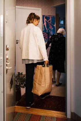 IMAGO Creative: Internationaler Frauentag, Mental Load und Care-Arbeit Female healthcare worker with shopping bag entering in house behind senior woman Sweden, Gothenburg, model released, property released Copyright: xMaskotx , MA90649