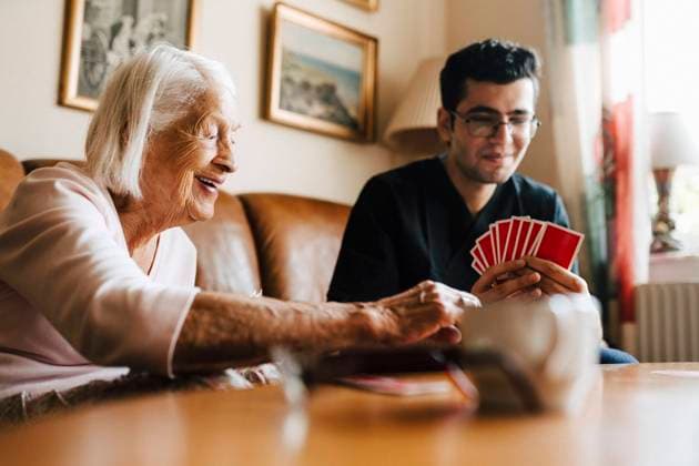 IMAGO Creative: Kollidierende Kulturen Happy senior woman playing cards with male healthcare worker in living room Sweden, Gothenburg, model released, property released Copyright: xMaskotx , MA90720