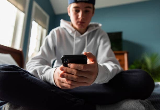 IMAGO Creative: Gesellschaft, Armut Low angle of teen boy in white sweater on smartphone in bedroom. Kingston, Ontario, Canada CR_DOHO211209E-877793-01 ,model released, Symbolfoto