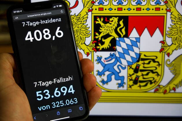Coronavirus in Deutschland - Covid-19-Dashboard des Robert Koch-Institut DEU, Deutschland, Bayern 12.12.2021: Die 7-Tage-Inzidenz für das Bundesland (Fälle letzte 7 Tage 100.000 EW) wird auf einem iPhone angezeigt, im Hintergrund das Landeswappen