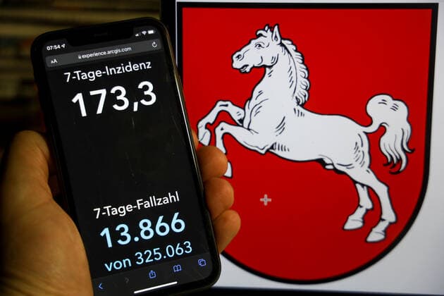 Coronavirus in Deutschland - Covid-19-Dashboard des Robert Koch-Institut DEU, Deutschland, Niedersachsen 12.12.2021: Die 7-Tage-Inzidenz für das Bundesland (Fälle letzte 7 Tage 100.000 EW) wird auf einem iPhone angezeigt, im Hintergrund das Landeswappen