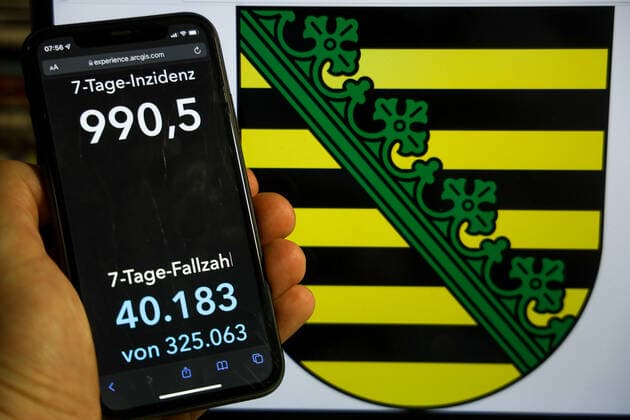 Coronavirus in Deutschland - Covid-19-Dashboard des Robert Koch-Institut DEU, Deutschland, Sachsen 12.12.2021: Die 7-Tage-Inzidenz für das Bundesland (Fälle letzte 7 Tage 100.000 EW) wird auf einem iPhone angezeigt, im Hintergrund das Landeswappen