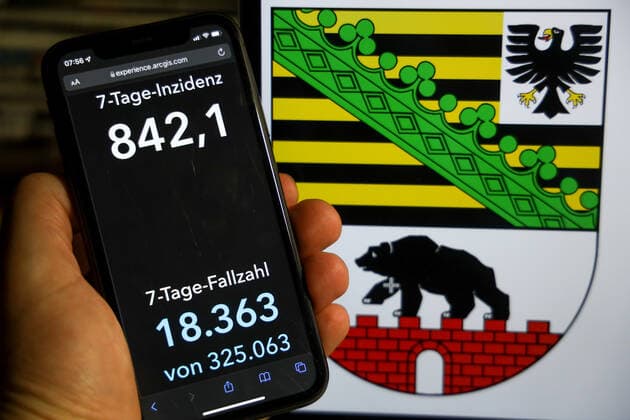 Coronavirus in Deutschland - Covid-19-Dashboard des Robert Koch-Institut DEU, Deutschland, Sachsen-Anhalt 12.12.2021: Die 7-Tage-Inzidenz für das Bundesland (Fälle letzte 7 Tage 100.000 EW) wird auf einem iPhone angezeigt, im Hintergrund das Landeswappen