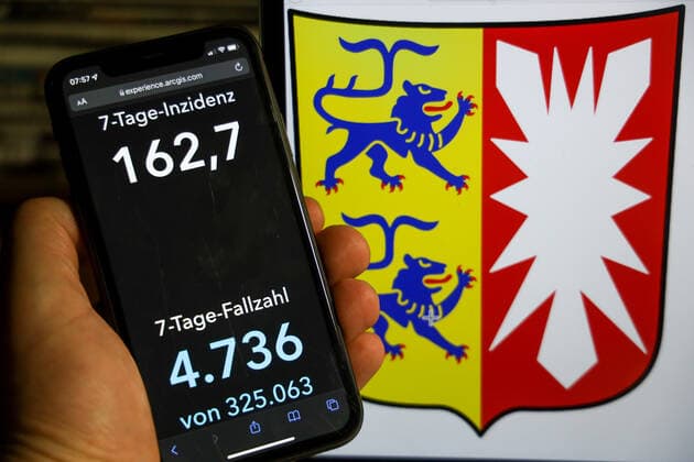 Coronavirus in Deutschland - Covid-19-Dashboard des Robert Koch-Institut DEU, Deutschland, Schleswig-Holstein 12.12.2021: Die 7-Tage-Inzidenz für das Bundesland (Fälle letzte 7 Tage 100.000 EW) wird auf einem iPhone angezeigt, im Hintergrund das Landeswappen