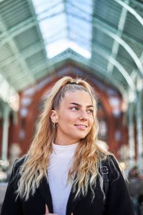 IMAGO Creative: Welttourismustag am 27. September Low angle of young female with blond curly hair wearing black coat standing in modern building, Model released AdalbertoRodriguez_AutumnYoungWoman_113.jpg Copyright: xAdalbertoxRodriguezx MR