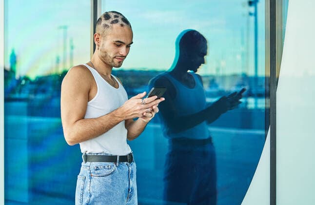 Creative Highlights Symbolbilder Positive eccentric male with dyed short hair leaning on glass wall and surfing mobile phone on city street, Model released AdalbertoRodriguez_SkatingFriends_69.jpg Copyright: xAdalbertoxRodriguezx MR