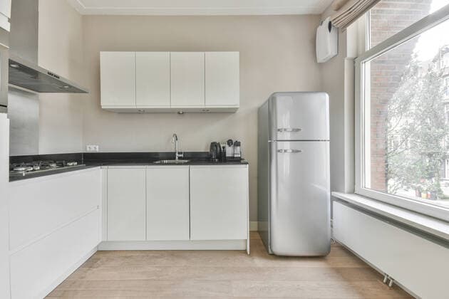 IMAGO Creative: Haushaltsger?te - K?hlschrank Interior of contemporary kitchen with white cabinets and built in oven metal range hood and fridge and wide window CasaMedia_VanBaerlenstraat_10.jpg Copyright: xCasaxMediax Model Released