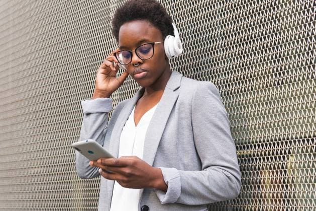 IMAGO Creative, Lifestyle, Tik Tok-Trend thatgirl Young African American female freelancer listening to podcast in headphones using smartphone standing at metal grid wall, Model released DavidMunoz_WendyLifestyle_46.jpg Copyright: xDavidxMunozx MR