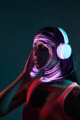 Creative Highlights Symbolbilder Charming Brazilian female listening to music in wireless headphones while standing with eyes closed in obscure studio on dark background with shadow of light on face, Model released ManuelRuiz_BrazilianWomanFluor_07.jpg Copyright: xManuelxRuizx MR