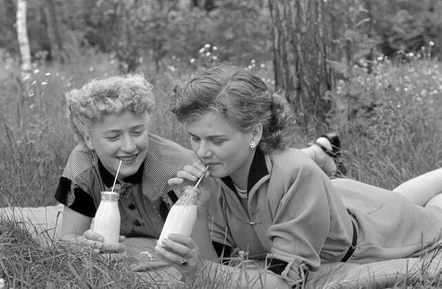 Milch trinkende Mädchen 1954 Girls drinking milk on a meadow Historisches Bild von zwei jungen Maedchen, die auf einer Wiese liegen und Milch trinken Young girls Women drinking milk, laying on a grasland, meadow. Happy and smiling beautiful young women enjoying a little bottle of milk with a straw