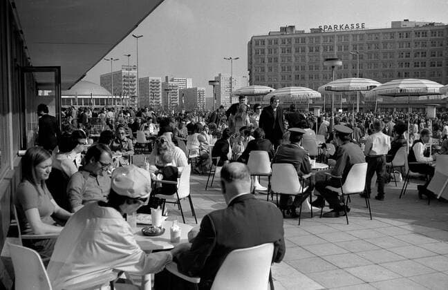 Eiscafe Berlin Alexanderplatz Historisches Bild und Foto: Eiscafe Berlin Alexanderplatz. Junge und erwachsene Menschen beim Eis essen. Im Hintergrund das HO Kaufhaus mit seiner Fassade. Historical Image and Photography: Eiscafe Berlin Alexanderplatz