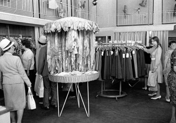 Bekleidungsgeschaeft 1963 Clothes shop 1963 Historisches Bild und Foto: Bekleidungsgeschaeft 1963. Frauen kaufen Kleider, Stoffe in einem Kleidungsladen. Anziehen, Mode der 1960er Jahre kaufen. An der Kasse stehen. Accessoires kaufen. Innenansicht Einzelhandelsgeschäft mit Regalen Historical Image and Photography: from a Clothes and Accessoires Shop.