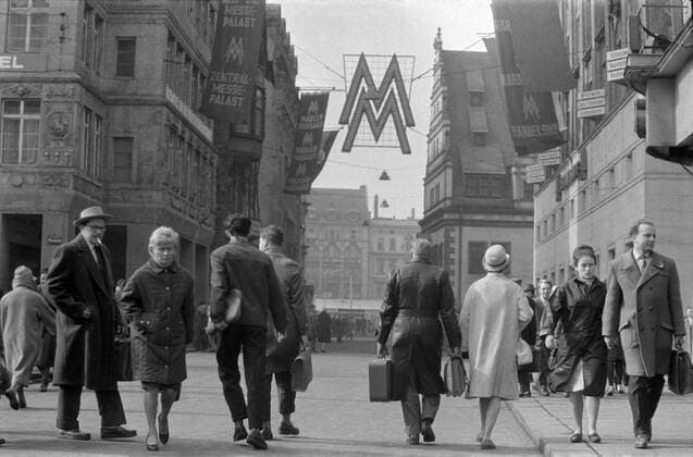 Handelshof Leipzig 1963 Historisches Bild und Foto: Leipziger Frühjahrsmesse 1963. Menschen flanieren vor dem Handelshof Leipzig 1963. Der Handelshof ist ein ehemaliges Messehaus in der Innenstadt von Leipzig, aktuell als Hotel genutzt Es steht an der Ostseite des Naschmarktes. Historical Image and Photography: People in front of the Handelshof Leipzig. The Handelshof is an old fair building in the city centre of Leipzig