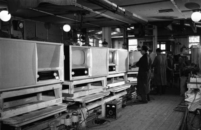 Television Factory in 1950 Historical Image of a television and radio factory in 1950 in east germany (GDR, DDR, VEB. Man Worker stand in a factory work room at the band conveyor and produce the first television in history.
