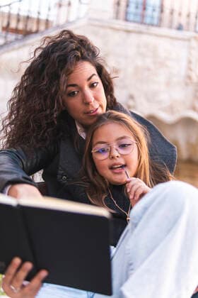 Woman teaching daughter over book in front of wall model released, JAQF00950