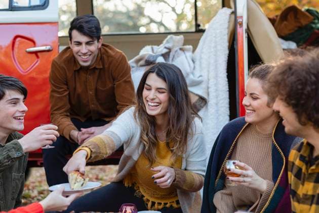 Cheerful woman serving cake to friends outside van on picnic model released, EIF02464