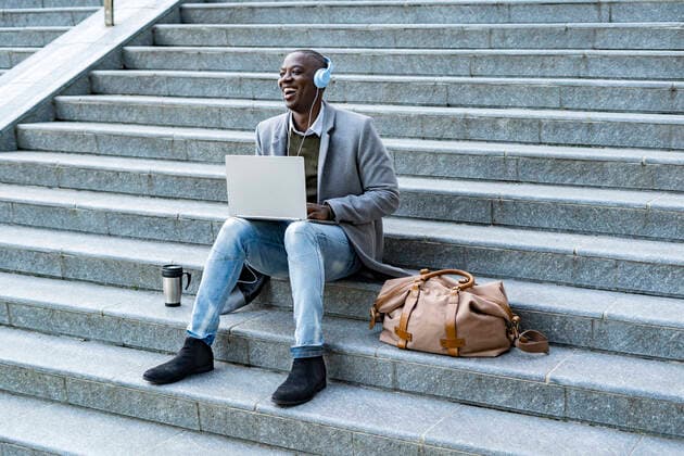 Laughing businessman with headphones sitting with laptop on steps model released, GIOF14415