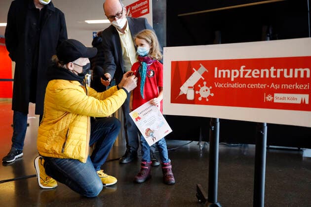 Thomas Baumgärtel und Dr. Johannes Nießen mit einem vollständig geimpten Kind mit Tapferkeitsurkunde bei der Vorstellung der Buttons mit der Impfbanane im Impfzentrum der Stadt Köln in der Lanxess-Arena. Hier werden auch Kinder (5-11 Jahre) geimpft. Vollständig geimpfte Kinder erhalten als Geschenk einen Button sowie eine Tapferkeitsurkunde. Die Buttons mit der Impfbanane sollen zudem an zahlreichen weiteren Impfstellen verteilt werden. Köln, 07.01.2022