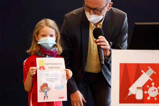 Dr. Johannes Nießen mit einem vollständig geimpften Kind mit Tapferkeitsurkunde bei der Vorstellung der Buttons von Thomas Baumgärtel mit der Impfbanane im Impfzentrum der Stadt Köln in der Lanxess-Arena. Hier werden auch Kinder (5-11 Jahre) geimpft. Vollständig geimpfte Kinder erhalten als Geschenk einen Button sowie eine Tapferkeitsurkunde. Die Buttons mit der Impfbanane sollen zudem an zahlreichen weiteren Impfstellen verteilt werden. Köln, 07.01.2022