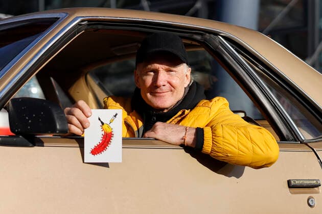 Thomas Baumgärtel in seinem Auto bei der Vorstellung der Buttons mit der Impfbanane im Impfzentrum der Stadt Köln in der Lanxess-Arena. Hier werden auch Kinder (5-11 Jahre) geimpft. Vollständig geimpfte Kinder erhalten als Geschenk einen Button sowie eine Tapferkeitsurkunde. Die Buttons mit der Impfbanane sollen zudem an zahlreichen weiteren Impfstellen verteilt werden. Köln, 07.01.2022