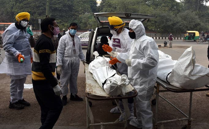 NEW DELHI, INDIA - JANUARY 13: Shaheed Bhagat Singh Sewa Dal volunteers in personal protective equipment (PPE) take out from a hearse the body of a person who died due to the Covid-19 coronavirus, at a cremation ground at crematorium Center Old Seema Puri Ghat, on January 13, 2022 in New Delhi, India. (Photo by Sonu Mehta Hindustan Times ) Daily Life Amid Coronavirus Pandemic In India