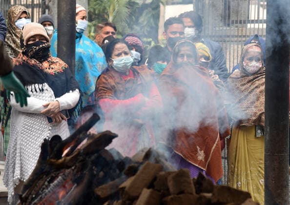 NEW DELHI, INDIA - JANUARY 13: Relatives and friends stand next to the funeral pyre of a person who died due to the Covid-19 coronavirus, disease at crematorium center Old Seema Puri Ghat, on January 13, 2022 in New Delhi, India. (Photo by Sonu Mehta Hindustan Times ) Daily Life Amid Coronavirus Pandemic In India