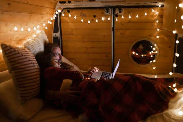 IMAGO Creative: Herbst, Touren mit dem Camper Young couple using laptop lying on bed in motor home model released property released, EGHF00304