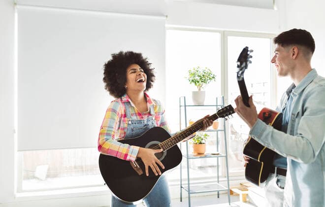 IMAGO Creative: Bildung, Musikerziehung Cheerful young couple playing guitar together at home model released property released, JCCMF05034