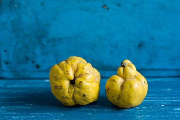 Studio shot of two ripe quinces lying on blue wooden surface, ASF06803