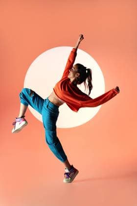 Side view of energetic happy female dancer jumping with raised leg and outstretched arms in light of projector in studio looking away, Model released ManuelRuiz_DancerWhiteStudio_09.jpg Copyright: xManuelxRuizx MR