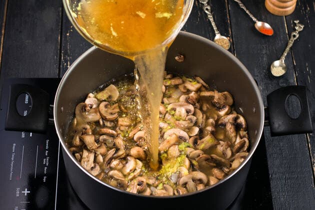 From above of broth pouring into metal pot with mushrooms on modern induction cooker while cooking soup near various spices MaxiGagliano_MushroomsSoup_5.jpg Copyright: xMaxixGaglianox Model Released