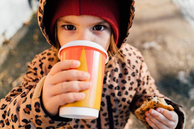 IMAGO Creative: Wintersport, Mode From above cute girl in warm clothes holding cookie and cup of takeaway drink while looking at camera in the street in winter day, Model released OleksandraTroian_KidOutdoorsInWinter_16.jpg Copyright: xOleksandraxTroianx MR