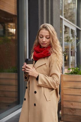 portrait of caucasian woman in beige trench coat outdoors with cup of coffee portrait of beautiful young caucasian woman in beige trench coat and red scarf with blond long hair standing outdoors at fall, holding cup of coffee. attractive female walks. autumn chill, lifestyle Copyright: xx 42830560