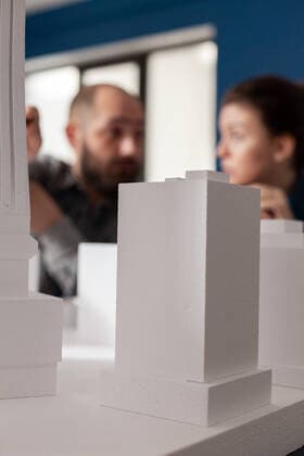 IMAGO Creative: Internationaler Tag der Architektur am 3. Oktober. Thema: Architektur zum Wohlfühlen Closeup of white foam architectural scale model of residential building complex Closeup of white foam architectural scale model of residential building complex in front of architects team working together. Detail of urban development project on design table. Copyright: xPhotographer:xDragosxCondreax 43265062
