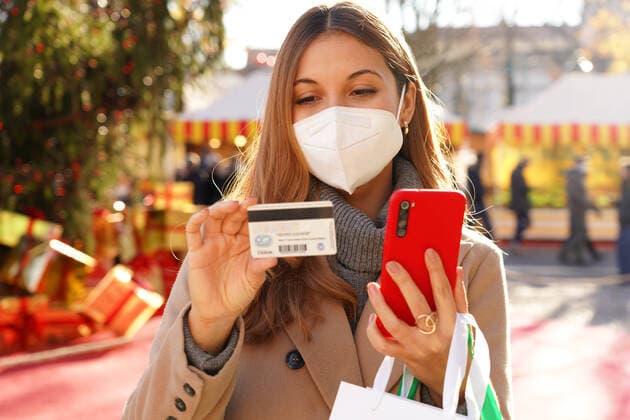 IMAGO Creative: Digitale Welt, Social Commerce Stylish woman with KN95 FFP2 protective mask watching credit card number to insert on smartphone for online payment with Christmas markets on the background Copyright: xx 43433888