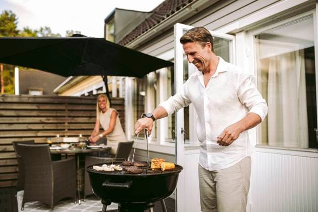 Smiling mature man preparing barbecue meal while in woman in background at back yard Sweden, Gothenburg, model released, property released Copyright: xMaskotx , MA91506