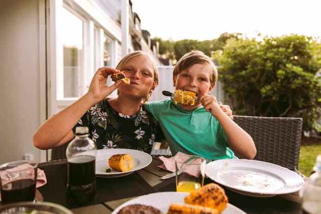 IMAGO Kreativ: Bruderschaft Portrait of siblings eating grilled corn and meat while sitting in back yard Sweden, Gothenburg, model released, property released Copyright: xMaskotx , MA91508