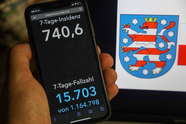 Coronavirus in Deutschland - Covid-19-Dashboard des Robert Koch-Institut DEU, Deutschland, Thüringen 06.02.2022: Die 7-Tage-Inzidenz für das Bundesland (Fälle letzte 7 Tage 100.000 EW) wird auf einem iPhone angezeigt, im Hintergrund das Landeswappen