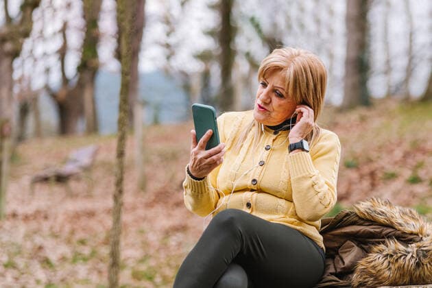 Focused middle aged female in earphones browsing modern cellphone while sitting in park with trees on blurred background HodeiUnzueta_AdultWomanPark_17.jpg Copyright: xHodeixUnzuetax Model Released