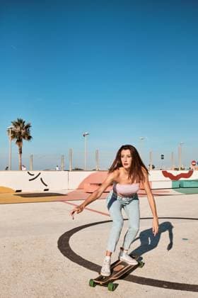 IMAGO Creative: Sommer, Sommertage im Stadtpark Full body of focused slim young female with long dark hair wearing top and jeans riding longboard in skate park in sunny summer day and looking away, Model released ManuelOrts_SkateYoungWoman_4.jpg Copyright: xManuelxOrtsx MR