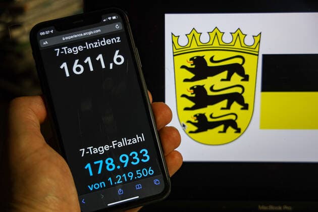 Coronavirus in Deutschland - Covid-19-Dashboard des Robert Koch-Institut DEU, Deutschland, Baden-Württemberg 13.02.2022: Die 7-Tage-Inzidenz für das Bundesland (Fälle letzte 7 Tage 100.000 EW) wird auf einem iPhone angezeigt, im Hintergrund das Landeswappen