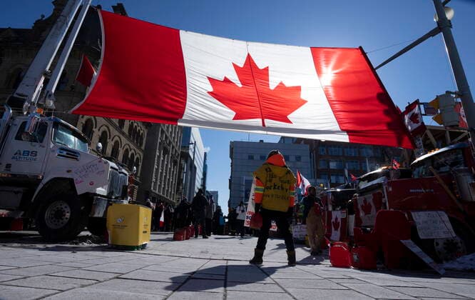 February 14, 2022, Ottawa, ON, Canada: A protester stands under a giant Canadian flag, Monday, Feb. 14, 2022 in Ottawa. The protesters are decrying federal vaccine mandates and provincial COVID-19 restrictions aimed at slowing the spread of the virus, some of which are being rolled back by provinces. Ottawa Canada  - ZUMAc35_ 20220214_zaf_c35_115 Copyright: xAdrianxWyldx