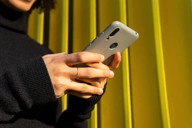 IMAGO Creative: Digitale Welt, Social Commerce Cropped unrecognizable African American female in black sweater text messaging on modern cellphone while standing near metal green wall on street DavidMunoz_DanyerisGlorias_27.jpg Copyright: xDavidxMunozx Model Released
