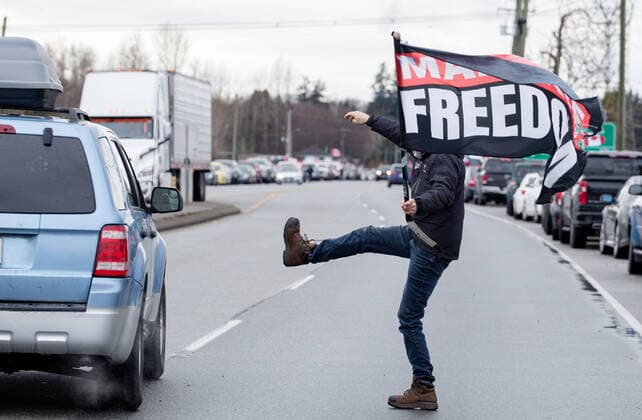 February 19, 2027, Surrey, British Columbia, Canada: A person holding a mandate freedom flag kicks at the car of a reporter as they leave the rally at Hwy 15 and 8th ave in Surrey, BC. Surrey Canada - ZUMA Pho 20270219_mda_w171_704 Copyright: xRyanxWalterxWagnerx