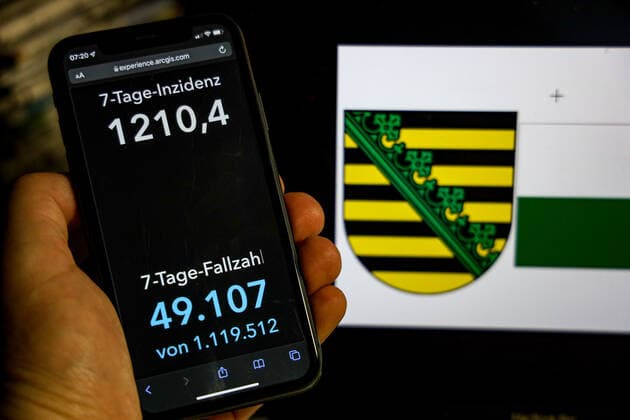 Coronavirus in Deutschland - Covid-19-Dashboard des Robert Koch-Institut DEU, Deutschland, Sachsen 20.02.2022: Die 7-Tage-Inzidenz für das Bundesland (Fälle letzte 7 Tage 100.000 EW) wird auf einem iPhone angezeigt, im Hintergrund das Landeswappen